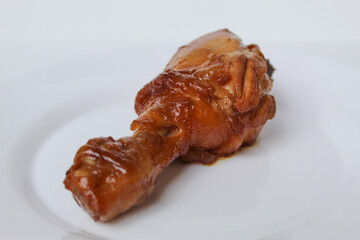 Ayam Kecap, or chicken cooked with sweet soy sauce. One chicken drumstick on white plate, isolated on white background
