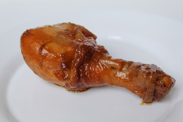 Ayam Kecap, or chicken cooked with sweet soy sauce. One chicken drumstick on white plate, isolated on white background
