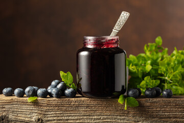Jar of blueberry jam with fresh berries on an old wooden table.