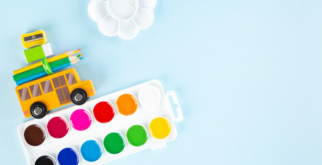 Back to school concept. Drawing accessories. Toy school bus drives watercolor, on blue background. Top view. Copy space