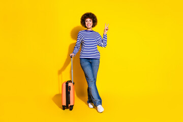 Full length photo of cheerful woman dressed striped shirt holding valise showing v-sign symbol...