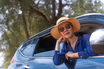 Happy beautiful asian woman enjoy travel in summer day, She looking out of car window to camera on beach road side. Outdoor lifestyle activity on road trip vacation concept.