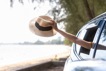 Close up of woman hand holding hat out of the car window with beach background. Outdoor lifestyle...