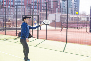 One woman with racquet and ball behind the net in paddle tennis court ready for training