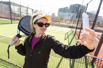 Young female smiling and looking at camera while playing padel against green background 