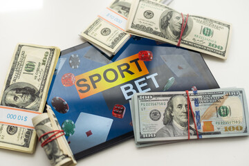 tablet pc with app for sport bets, on top of stacks of banknotes, white background, concept of...