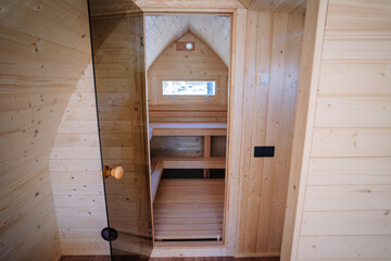 Interior view of a small wooden room featuring a built-in wooden staircase leading to a loft area, with an arched window at the end.