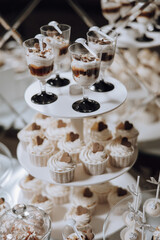 A white cake stand with a variety of cupcakes and desserts on it. The desserts are decorated with hearts and other designs, giving the impression of a special occasion or celebration