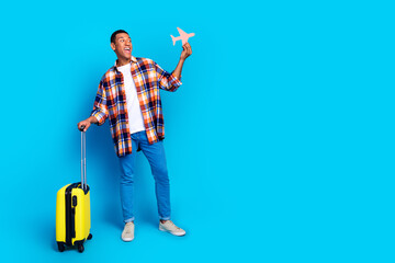 Full size photo of nice young man suitcase little plane empty space wear shirt isolated on blue...