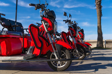 Close-up of red three-wheeled electric scooters on a blue sky background on a sunny day. Rent...