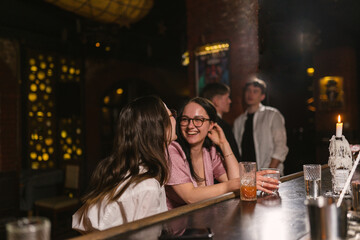 Fashionable brunette girls have fun after work at bar counter with candles. Guests spend time at...