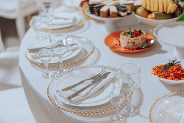 A table with a white tablecloth and a variety of food and drinks. The table is set with silverware...