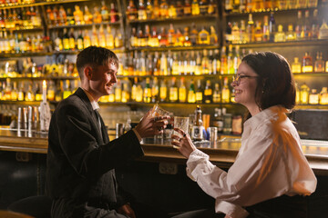 Young people smile and raise glasses with alcohol up in pleasant meeting. Happy couple have fun...