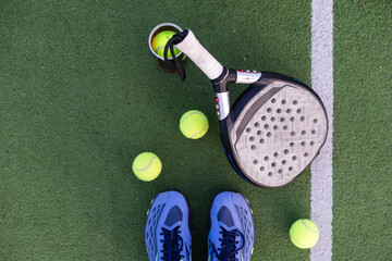 Yellow balls on grass turf near padel tennis racket behind net in green court outdoors with natural...