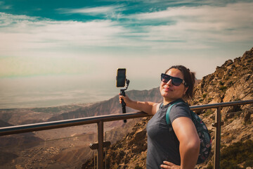Woman on the mountain films the view of the mountains with her phone camera