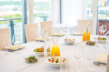 Served table with appetizers, salads and juice on a sunny day in a panoramic restaurant.