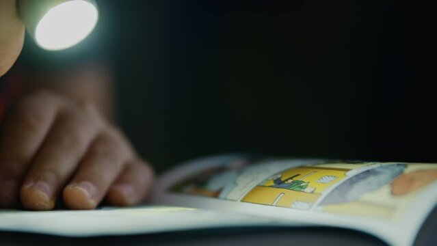 Boy shining a flashlight at a comic book outdoors at night