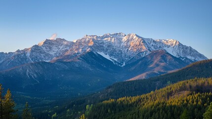 Sunrise over snow-capped mountain range with forested valley. Golden light on peaks.