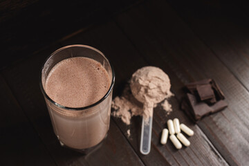 Protein milkshake cocktail in a glass, plastic measuring spoon with whey protein powder, white...