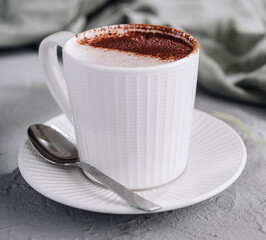 Fresh cappuccino in a white cup on a gray surface