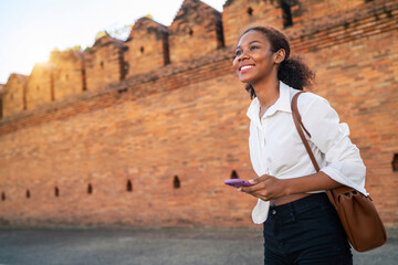 black girl holding phone ancient area finding location on holiday. female teenage tourist holding...