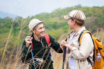 active asian senior couple hiking together on summer time,they are look at each other and smiling,concept of elderly pensioner lifestyle,family relationship,activity,travel,adventure in nature