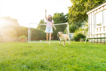Cheerful young woman playing with dog, throwing a ball and have fun together. Happy family playing...