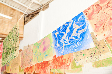 Colorful sheets of handmade paper freshly dyed with the marbling technique hanging from ropes to...