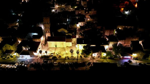 Drone flight along the embankment of the night city of Perast, protected by UNESCO and illuminated by warm evening lights