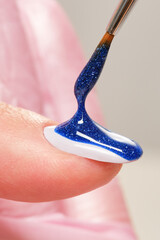 Close up process of applying blue pearlescent varnish. Blue glitter nail polish and brush, macro....