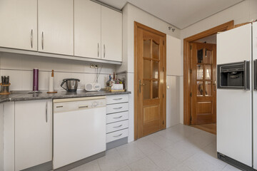 A kitchen with white cabinets, gray countertops, tiled backsplash and oak doors on two walls