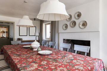A large dining table with rustic-style wooden chairs next to a fireplace with a red patterned...