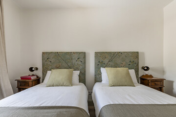 A bedroom with twin beds with headboards upholstered in printed fabric, n cushions and pillows and...