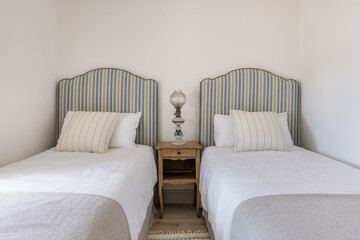 A bedroom with two single beds with headboards upholstered in striped fabric, matching cushions and...