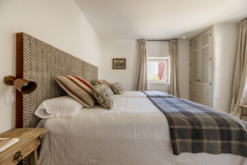 A nice bedroom with two single beds pushed together with a rustic-style fabric-upholstered headboard, fabric-upholstered blankets and cushions, and a built-in wardrobe in a corner