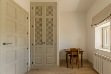 A room with a built-in wardrobe with wooden lattice doors and a vintage wooden desk with matching...