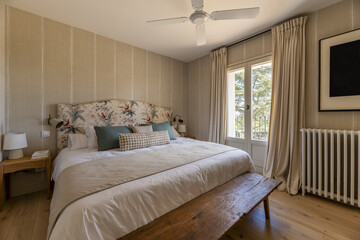 Bedroom with king size bed with fabric upholstered headboard, blankets and many cushions and...