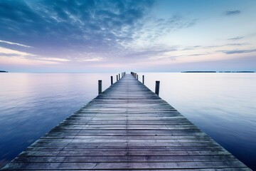 A serene coastal scene with a single wooden pier extending into a calm ocean at dawn, space for text