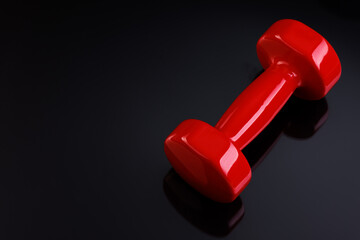 A red dumbbell lies on a black glass surface. View from above.