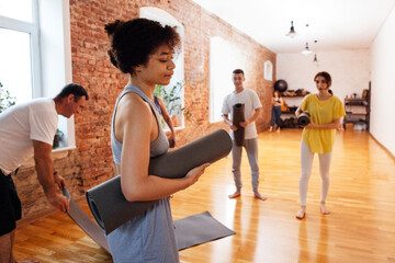 A group of multiethnic athletes roll up mats after yoga classes. The end of fitness classes and...