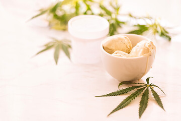 A hemp leaf is lying on a mock-up jars of ice cream on a white marble table
