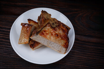 Roasted pork entrecote cut into pieces in a white plate on a wooden cutting board . Grilled pork entrecote. Pork steak.