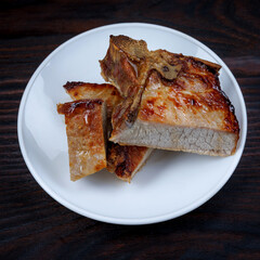 Roasted pork entrecote cut into pieces in a white plate on a wooden cutting board . Grilled pork entrecote. Pork steak.