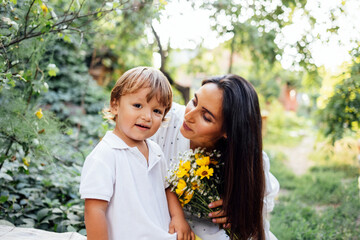 Attractive woman holds bouquet in her hands and looks at her child in garden.