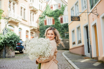 Portrait of beautiful young blonde woman with bouquet of white flowers in the center of European...