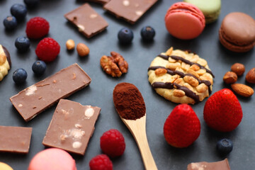Macarons, chocolate, cookies, berries and various nuts on dark blue background. Selective focus.
