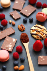 Macarons, chocolate, cookies, berries and various nuts on dark blue background. Selective focus.