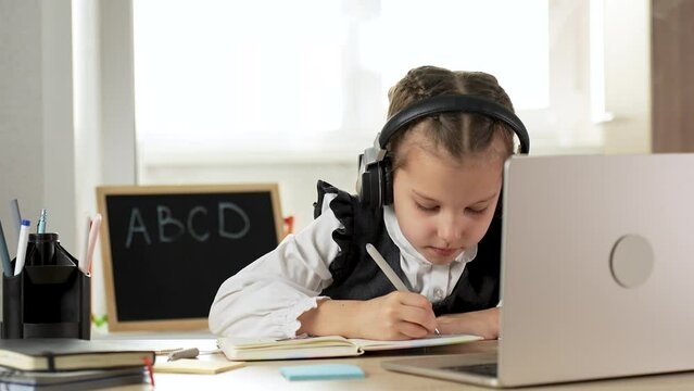 Caucasian child girl wear headphones, using laptop sitting writing listening tutor online virtual lesson