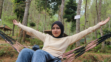 Young woman with headscarf resting in comfortable hammock at green garden