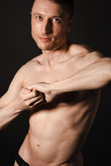 Naklejka premium A man with a beautiful body poses in the studio against a black background.